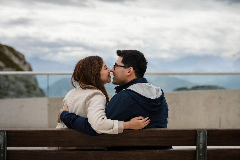 Mann und Frau sitzen auf einer Bank, küssen sich nach Verlobung